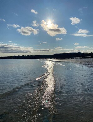 A body of water with a visible wake pattern, likely from a moving boat, under a clear sky with the sun shining. - Bay Area House, Spiddal (Spiddal)