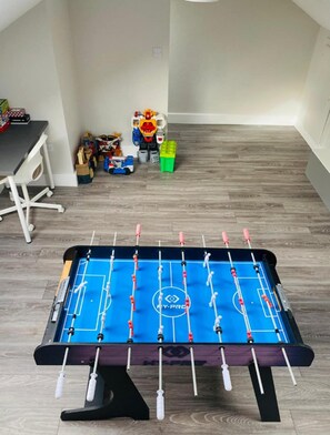 Ein Zimmer mit einem Kicker, einem Schreibtisch und Spielzeug auf dem Boden.