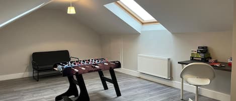 A room with a foosball table, a black chair, a white office chair, a skylight, and a radiator.