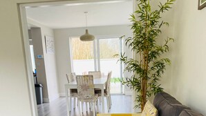 A modern living room with a grey sofa, yellow patterned cushions, a dining area with a white table and chairs, and a tall bamboo plant. - Bay Area House is a perfect base to tour Connemara (Spiddal)
