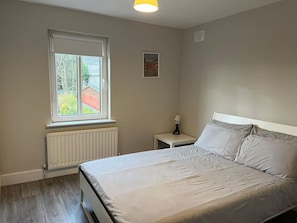 A bedroom with a bed, a window, a radiator, and a nightstand with a lamp.