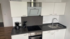 Uma cozinha moderna com armários brancos, micro-ondas embutido, fogão a gás, forno e pia.