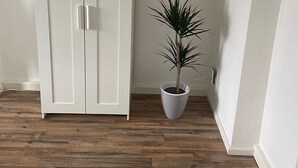 Quarto com guarda-roupa branco, planta em vaso e chão de madeira.