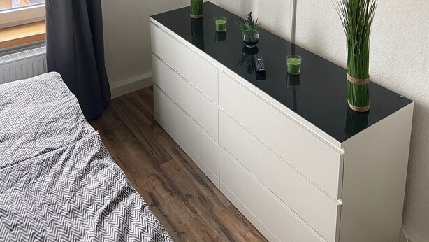 Quarto moderno com cama, penteadeira, televisão na parede e janela com cortina.
