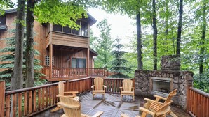 Una terraza de madera con sillas Adirondack, una chimenea de piedra y una cabaña con balcón.
