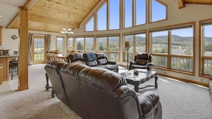 Ein geräumiges Wohnzimmer mit Ledersofas, einem Essbereich und großen Fenstern mit Blick auf die Landschaft.