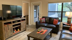 Ein Wohnzimmer mit Fernseher auf einem Holzboden, einer Ledersofa und einem Couchtisch.