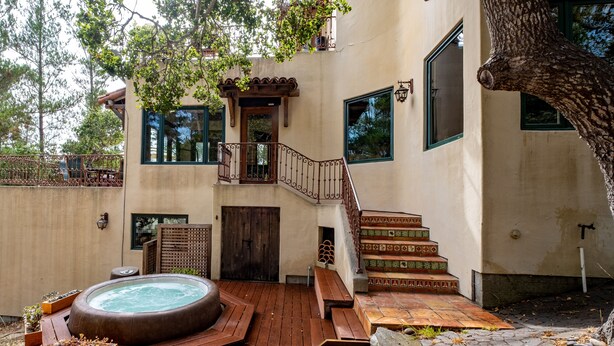A spa area with a hot tub, wooden deck, and a staircase leading to a balcony. - Custom Built Rental on Lodge Hill! Stunning Home in a Peaceful Neighborhood! (Cambria)