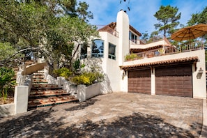 A two-story house with a tiled driveway, a staircase with red and white tiles, and a brown garage door.