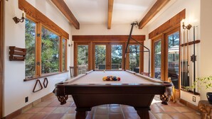 A pool table in a room with large windows, wooden beams, and a view of trees. - Custom Built Rental on Lodge Hill! Stunning Home in a Peaceful Neighborhood! (Cambria)