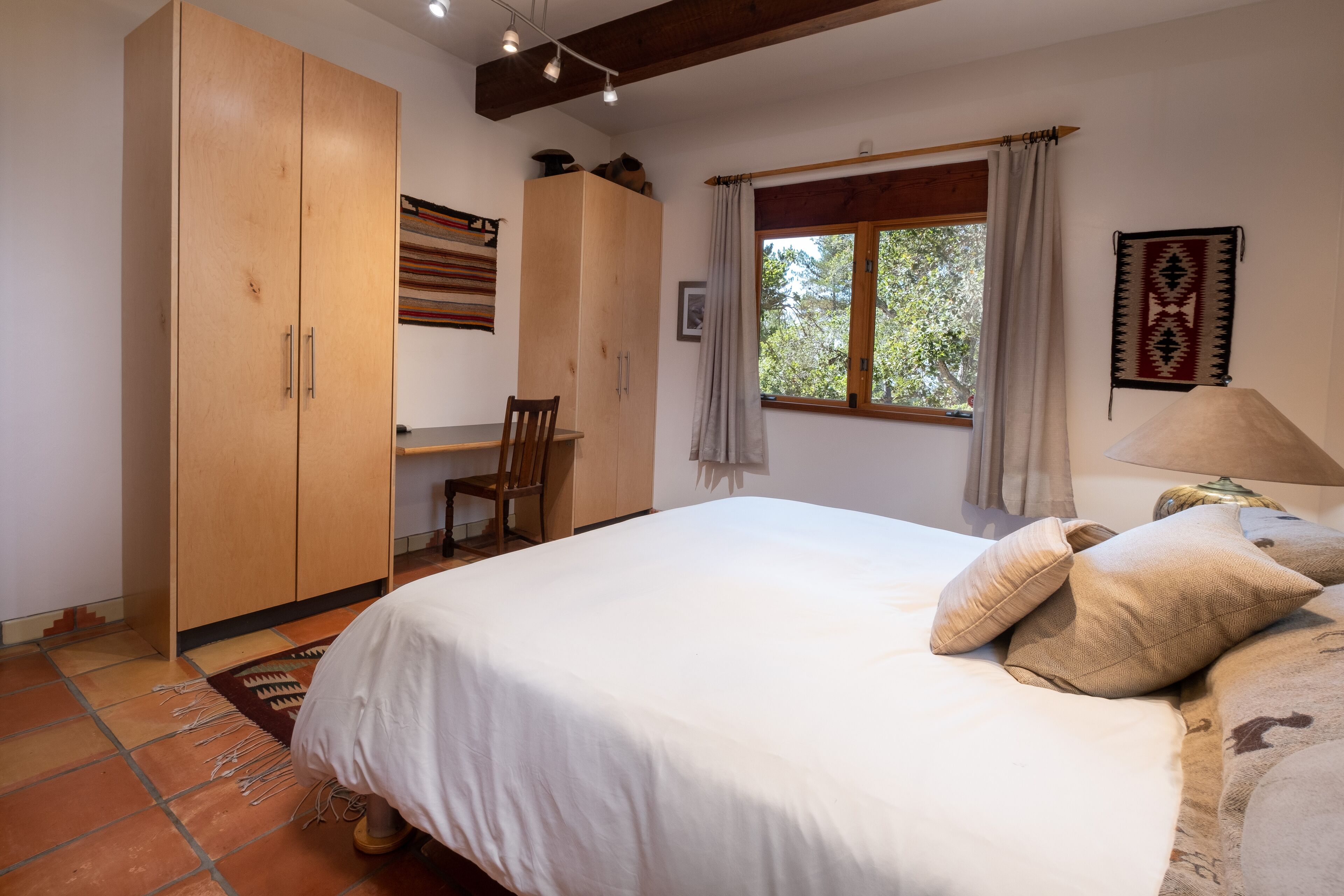 Une chambre à coucher avec un grand lit, une armoire en bois, un bureau et une fenêtre avec des rideaux.