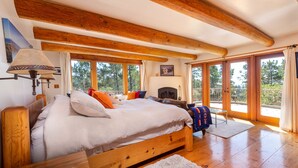 A bedroom with a wooden bed, a fireplace, and large windows. - Custom Built Rental on Lodge Hill! Stunning Home in a Peaceful Neighborhood! (Cambria)