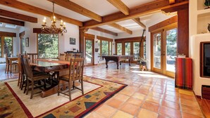 A spacious room with a wooden dining table, chairs, a fireplace, and large windows. - Custom Built Rental on Lodge Hill! Stunning Home in a Peaceful Neighborhood! (Cambria)