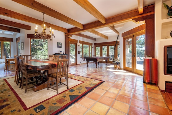 A spacious room with a wooden dining table, chairs, a fireplace, and large windows.