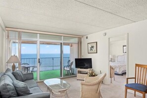 Relax in this spacious living area with a comfortable sofa, flat-screen TV, and sliding glass door leading to a balcony with ocean views.
