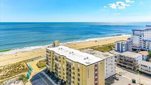 Un hotel frente a la playa con varios pisos, un estacionamiento y vista al mar.
