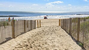 Un sendero de arena bordeado por una valla de madera a ambos lados, que lleva al océano.