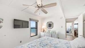 Un dormitorio con cama, ventilador de techo, televisor, cómoda y vista al océano.