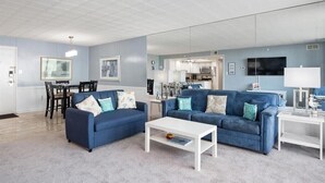 Ein modernes Wohnzimmer mit zwei blauen Sofas, einem weißen Couchtisch und einem Essbereich mit Tisch und Stühlen.
