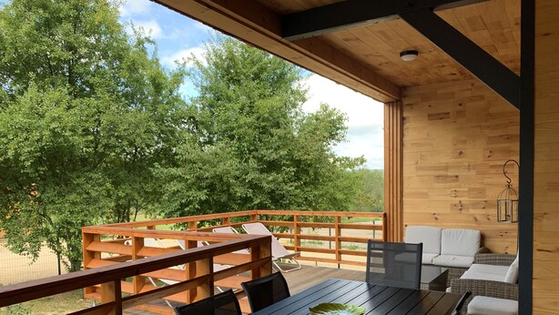 Une terrasse en bois avec une table et des chaises, donnant sur un espace verdoyant planté d’arbres.