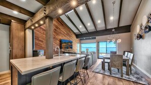 A modern kitchen with a central island, bar stools, and a dining area with a table and chairs. - Stunning Lakefront Near Heavenly LLV611 (South Lake Tahoe)