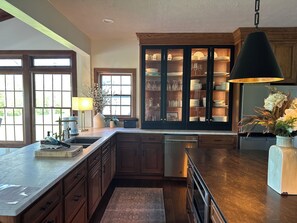 Une cuisine avec des meubles de rangement en bois, un îlot central intégré, une grande fenêtre et un luminaire suspendu.