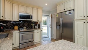 A kitchen with white cabinets, a stainless steel refrigerator, a microwave, and a granite countertop. - Pet Friendly Cottage Minutes from the KB Pier (Kure Beach)