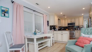 A kitchen with white cabinets, a dining table with chairs, and a teal armchair. - Pet Friendly Cottage Minutes from the KB Pier (Kure Beach)