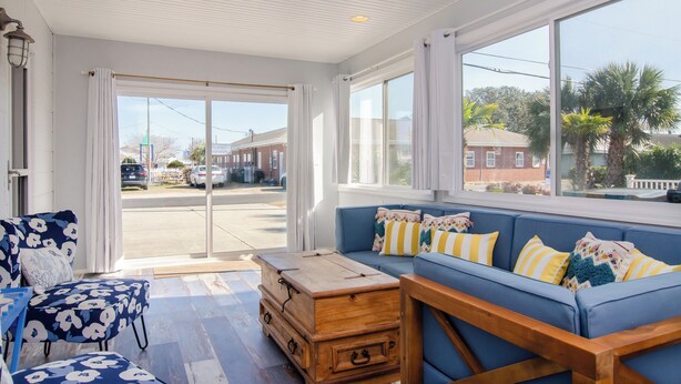A room with a large window, a blue sofa with patterned cushions, a wooden chest of drawers, and a ceiling fan. - Pet Friendly Cottage Minutes from the KB Pier (Kure Beach)