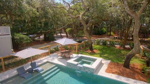 A swimming pool with a hot tub, surrounded by trees and a patio area with chairs and umbrellas. - "Driftwood" in S. Forest Beach! (Hilton Head Island)