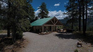 Une cabane en rondins surmontée d’un toit végétalisé, entourée d’arbres et bordée d’une allée en gravier.