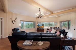 A spacious living room with a black leather sofa, a wooden coffee table, and a television.