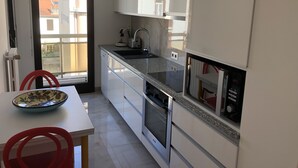 A modern kitchen with white cabinets, a stainless steel sink, and a built-in oven. There is a window providing a view of the outside. - Azurie Sea View Apartment (juan les pins)