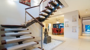 A modern staircase with a unique design, leading to a well-lit living area with a statue and a dining table.
