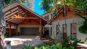 A modern house with a covered patio, a garage, and tropical vegetation.