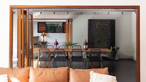A dining area with a wooden table and chairs, a sofa with cushions, and a decorative wall piece.