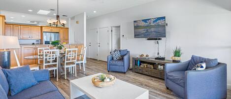 A spacious living area with a dining table, two sofas, a coffee table, and a TV mounted on the wall.