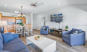 A spacious living area with a dining table, two sofas, a coffee table, and a TV mounted on the wall. - 150-4 Ocean Front Condo with an Amazing View! (Lahaina)