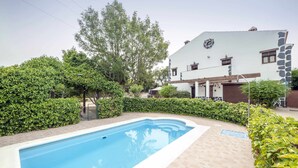Una piscina rodeada de setos y un edificio blanco con detalles de piedra.