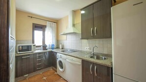 Una cocina compacta con armarios de madera oscura, una lavadora blanca, un microondas y un lavamanos de acero inoxidable.