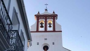 Un edificio blanco con una torre de campanas, una entrada arqueada grande y un pequeño balcón con barandilla de hierro forjado.