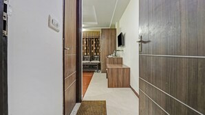 A hallway with a wooden door, a small table with a kettle, and a television mounted on the wall. - Treebo Mohit Regency (Bhopal)