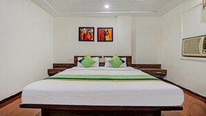 A hotel room with a bed, two paintings on the wall, and an air conditioning unit. - Treebo Mohit Regency (Bhopal)