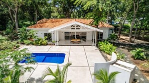 Een modern huis met een zwembad, overdekt terras en weelderige begroeiing.