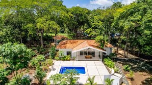 A house with a tiled roof, a swimming pool, and surrounded by dense greenery.