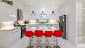 A modern kitchen with white cabinets, a central island with bar stools, stainless steel appliances, and pendant lighting.