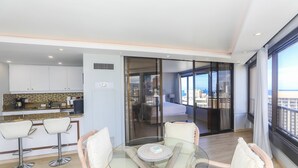 A modern kitchen with a bar area, a dining table with chairs, and a balcony with a city view. - 2-Bedroom Ocean View, Perfect Location In Wakiki (Honolulu)