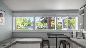 Ein Zimmer mit integriertem Sitzbereich, einem kleinen Tisch und einem Fenster mit Blick auf Bäume und parkende Autos.