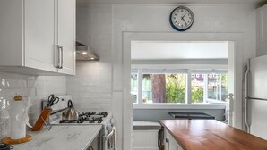 Eine moderne Küche mit weißen Schränken, einer Holz Arbeitsplatte, einem Gasherd und einem Fenster mit Blick nach draußen.