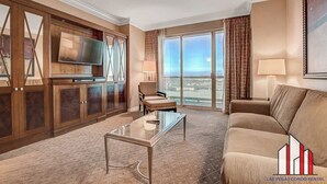 A spacious living room with a large TV, a glass coffee table, a sofa, and a view of the city through large windows. - MGM Signature-28-714 1BR 2-Bath Balcony Suite (Las Vegas)
